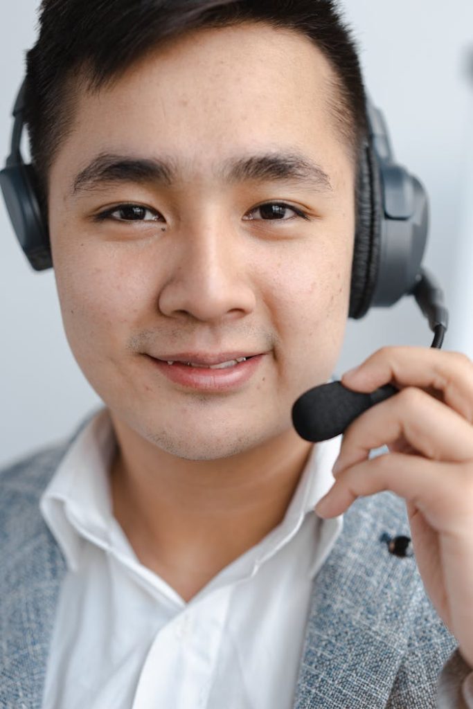 man-smiling-and-holding-microphone-of-the-headset-7681117 Close-up of a call center agent smiling while wearing a headset microphone.
