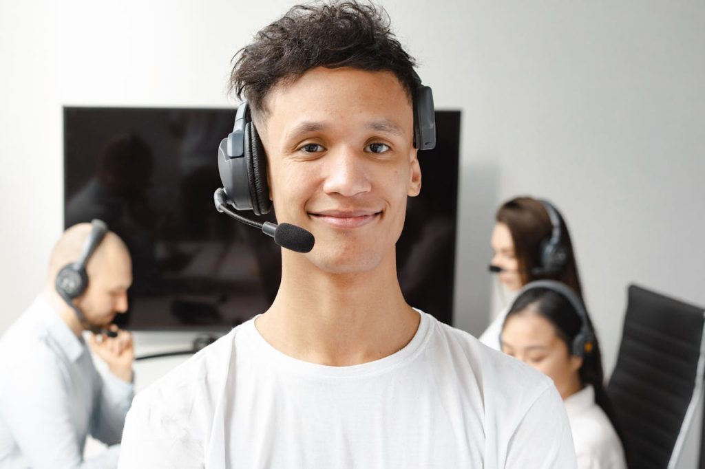 photograph-of-a-man-in-a-white-shirt-wearing-a-black-headset-7681842 Professional call center agent wearing a headset, smiling confidently in a modern office setting.